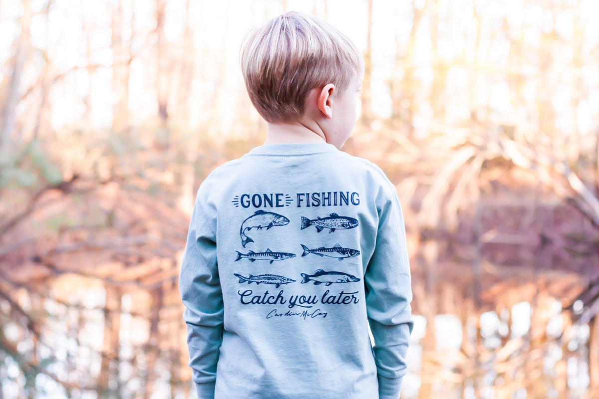 Child wearing a long-sleeve fishing tee beside the water