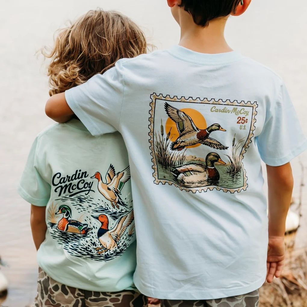 Two children wearing Cardin McCoy duck graphic tees by the water