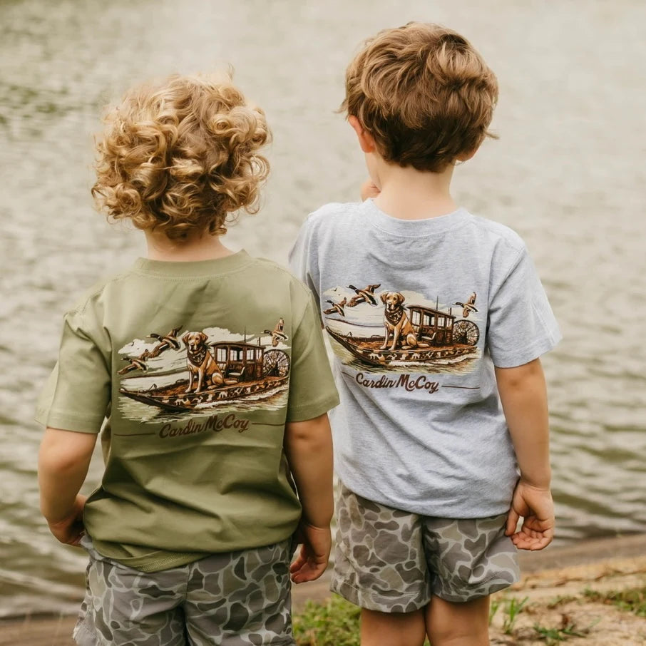 Two children wearing Cardin McCoy duck boat graphic tees beside the water.