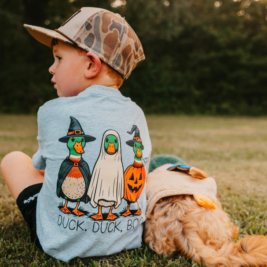 A child wearing a Duck, Duck, Boo tee beside a dog.
